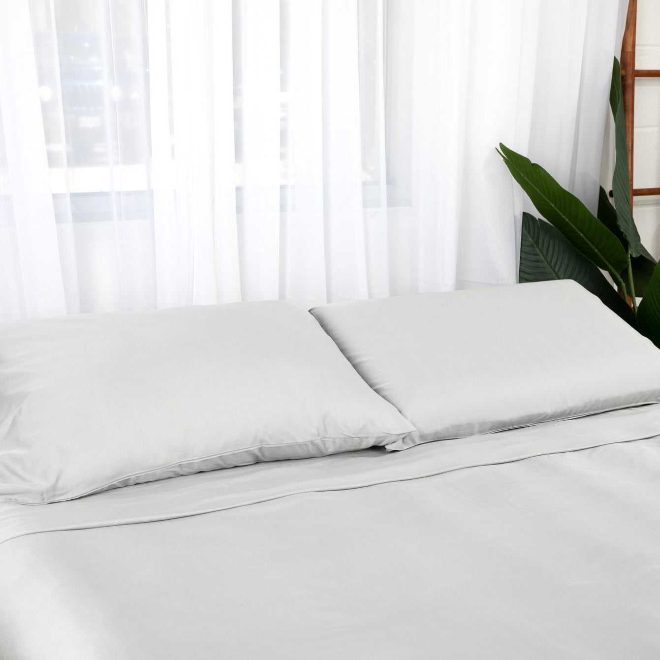 A neatly made white bed with two white Bamboo Viscose Pillowcase Set pillows in a bright bedroom.